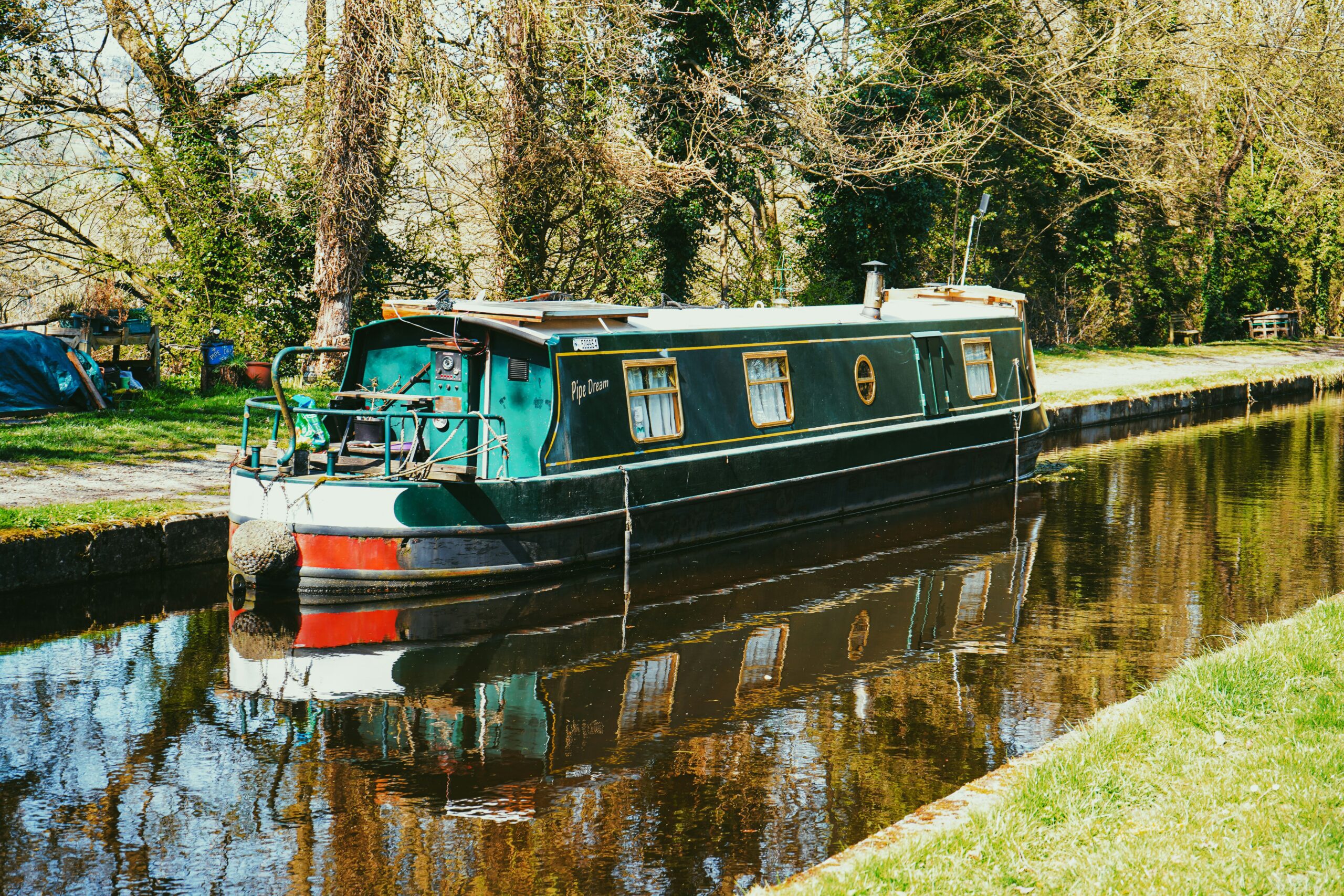 A green canal boat sat on the canal on a spring day